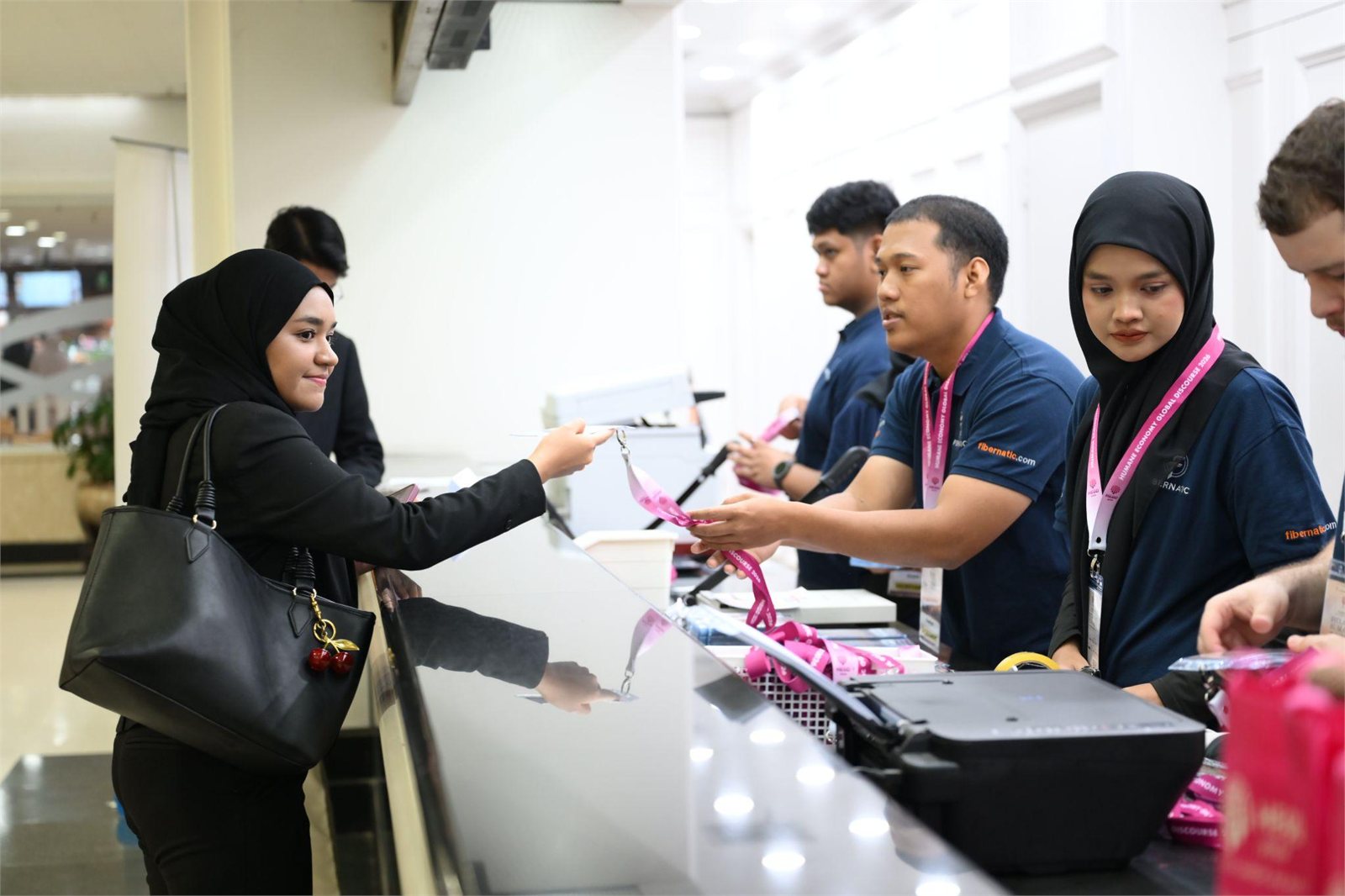 Fibernatic staff at the HEGD 2026 registration counter, handing a lanyard and printed name tag to an arriving attendee